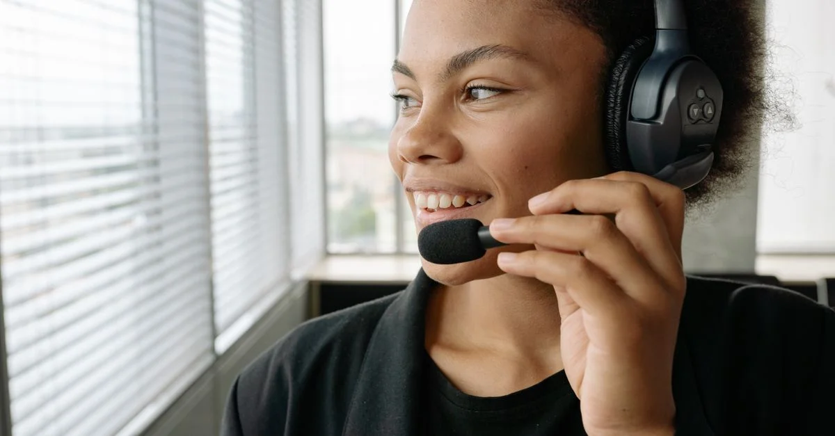 Afrikanisch-amerikanische Frau lächelnd und sprechend mit einem Headset in einem Bürosetting.