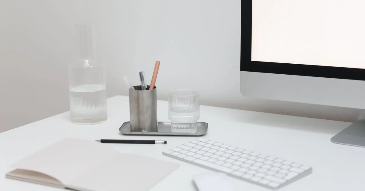 Minimalistischer Arbeitsplatz mit einem modernen Computer, Notizblock und Glaswaren auf einem stilvollen Schreibtisch.