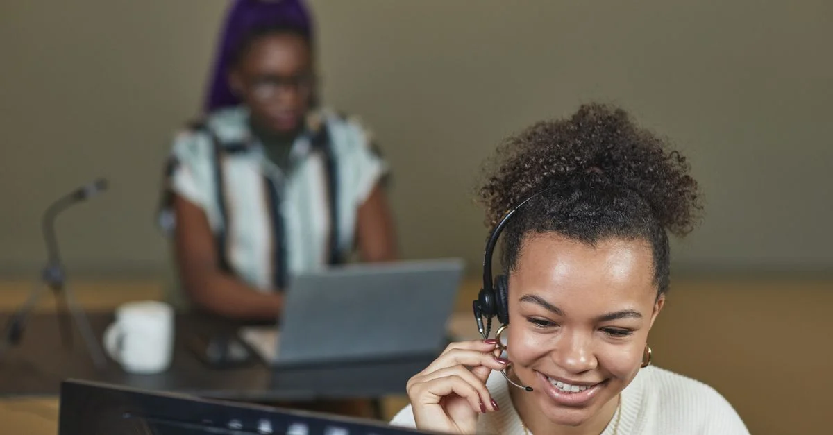 Lächelnde Frau, die ein Headset trägt und an einem Callcenter-Schreibtisch mit Laptop arbeitet.