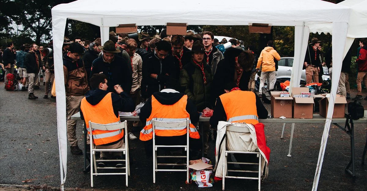 Überfülltes Outdoor-Check-in-Zelt bei einer Veranstaltung mit Teilnehmern in fluoreszierenden Westen und Pfadfinderuniformen.