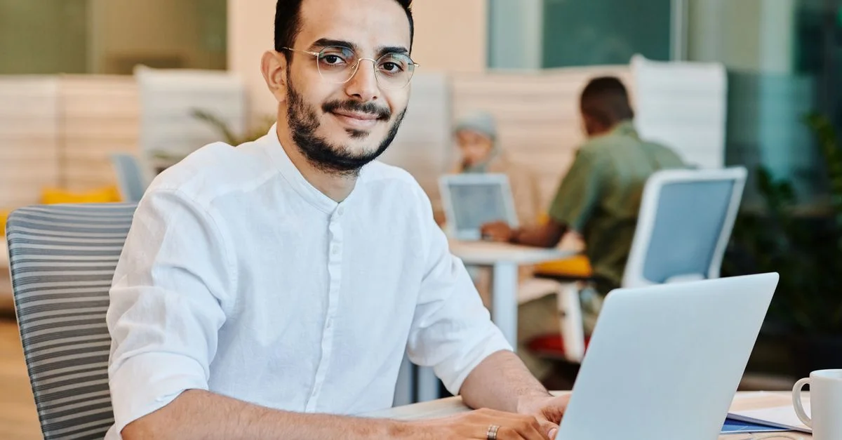 Asiatischer Mann mit Brille, der in einem hellen, modernen Arbeitsplatz an einem Laptop arbeitet und sich auf Aufgaben konzentriert.