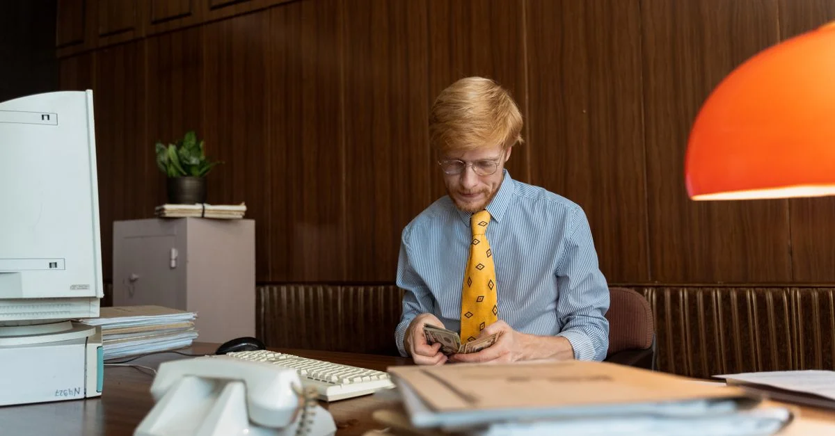 Ein Profi zählt Bargeld an einem retro Schreibtisch mit einem Computer und Akten.